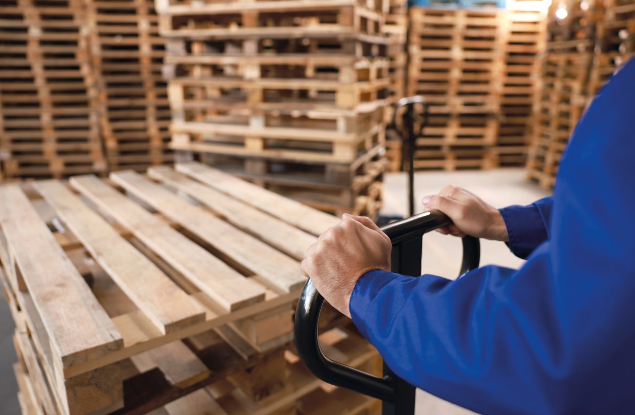 Worker moving wooden pallets with manual forklift in warehouse,