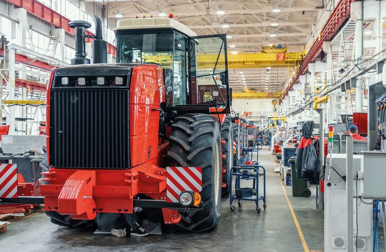 Big red harvester or tractor in process of being assembled on production line at factory for production manufacturing of agricultural machinery